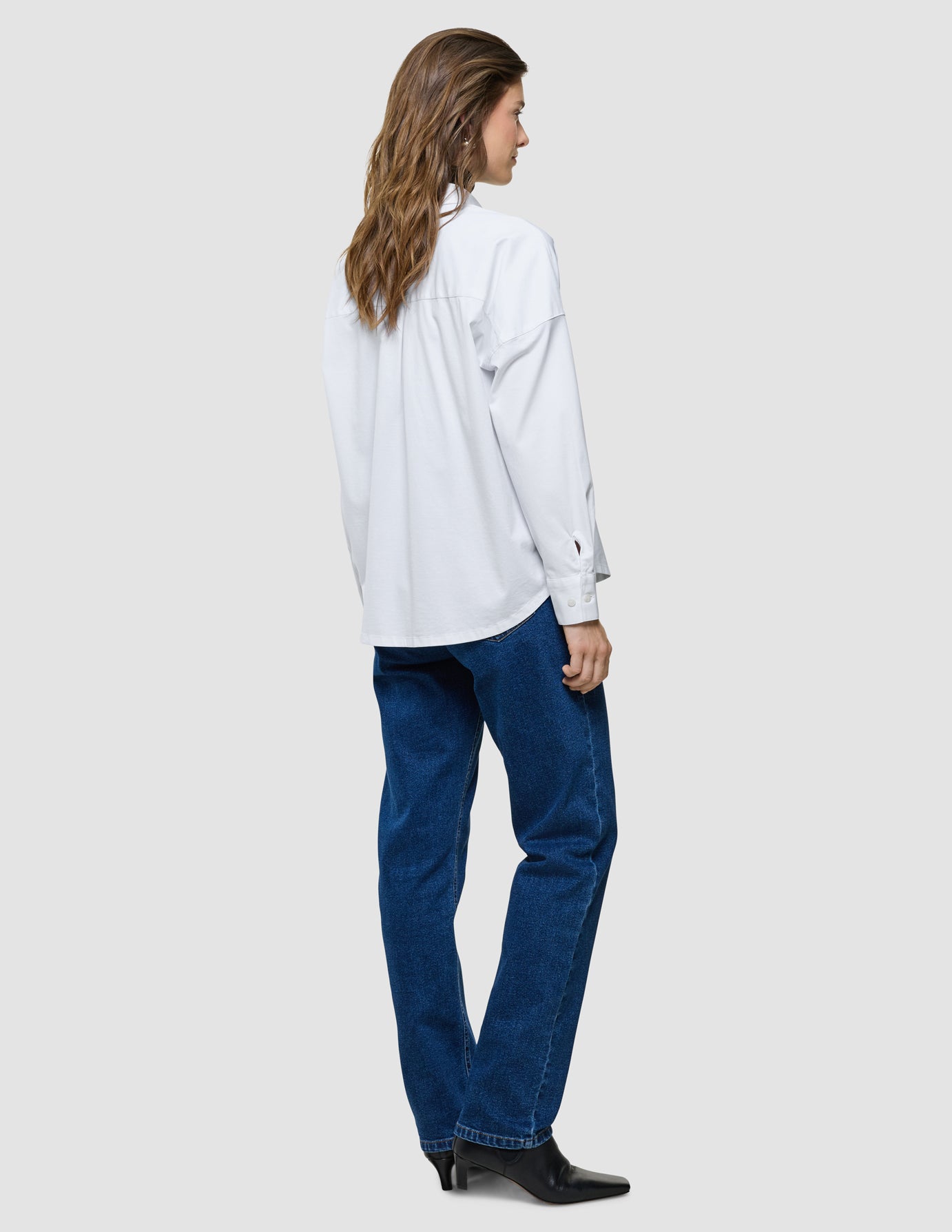 Oversized Long Sleeve Shirt i Off White, helfigur set bagfra af kvinde i hvid skjorte og blå jeans.